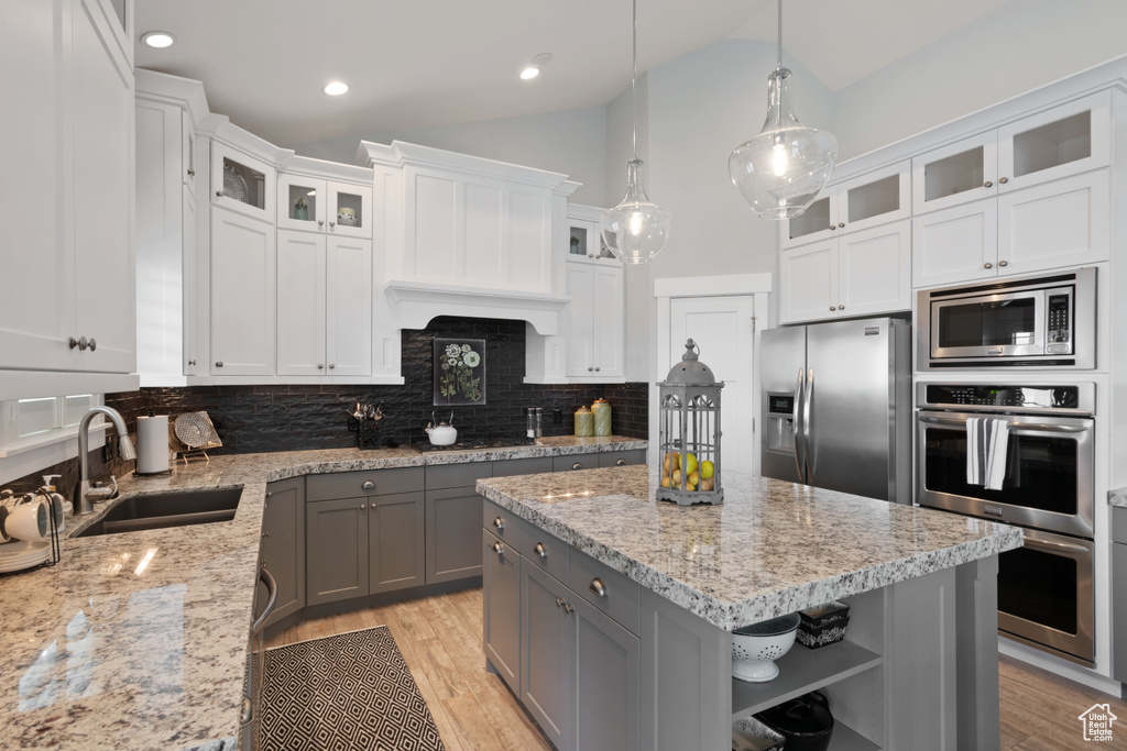 Kitchen featuring gray cabinetry, open shelves, appliances with stainless steel finishes, decorative backsplash, and a center island