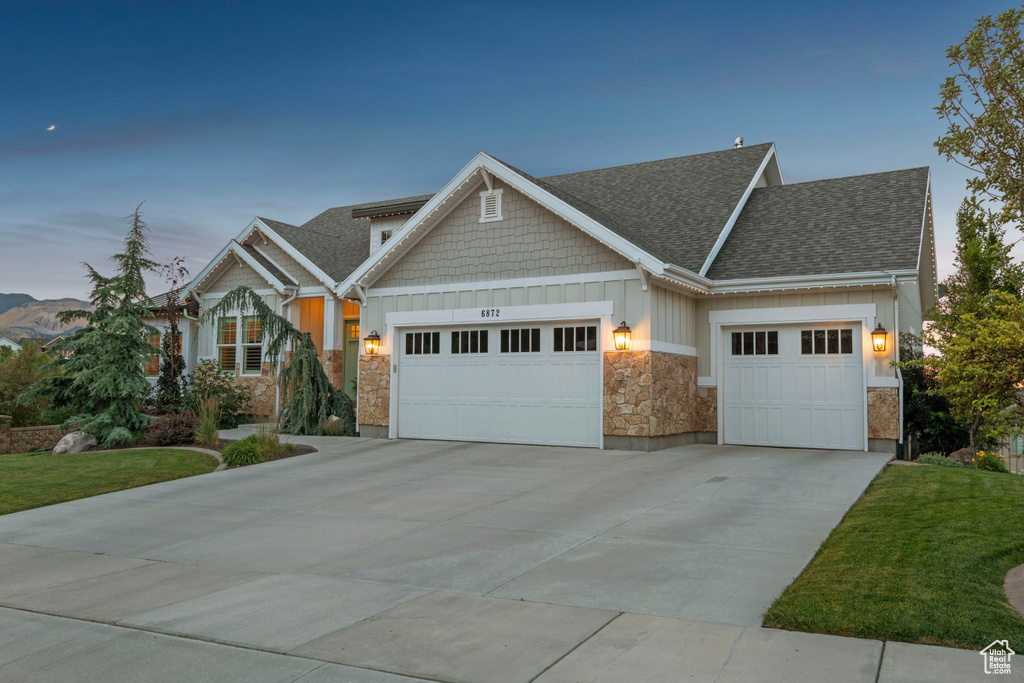 Craftsman house featuring an attached garage, board and batten siding, a shingled roof, stone siding, and driveway