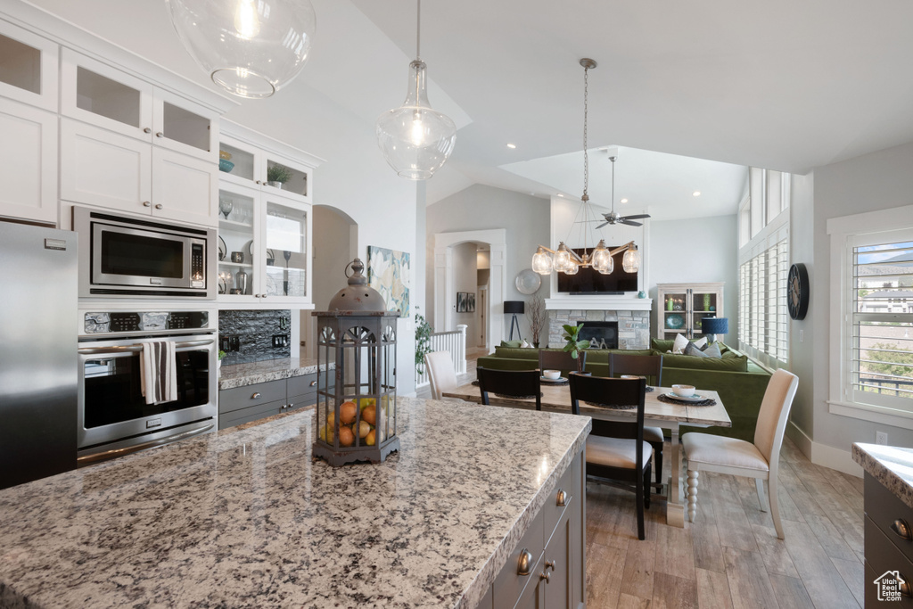 Kitchen with appliances with stainless steel finishes, a stone fireplace, light stone countertops, open floor plan, and gray cabinets