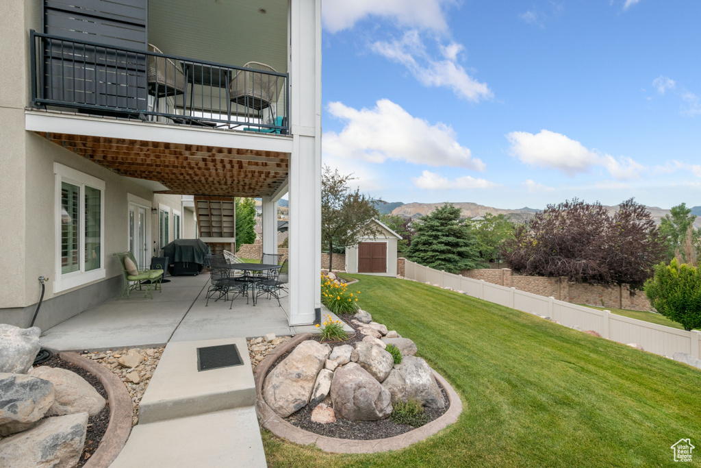 View of yard with a patio, a storage unit, a mountain view, outdoor dining area, and a balcony