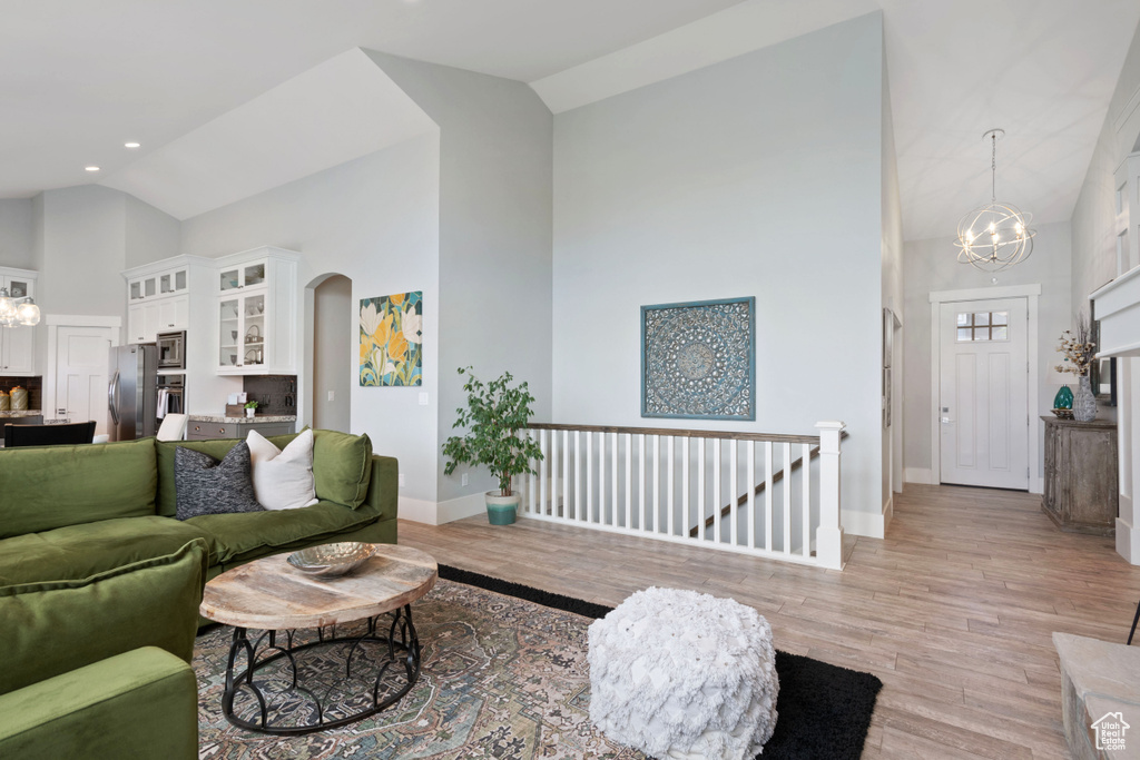 Living room featuring high vaulted ceiling, a chandelier, arched walkways, and light wood-style floors