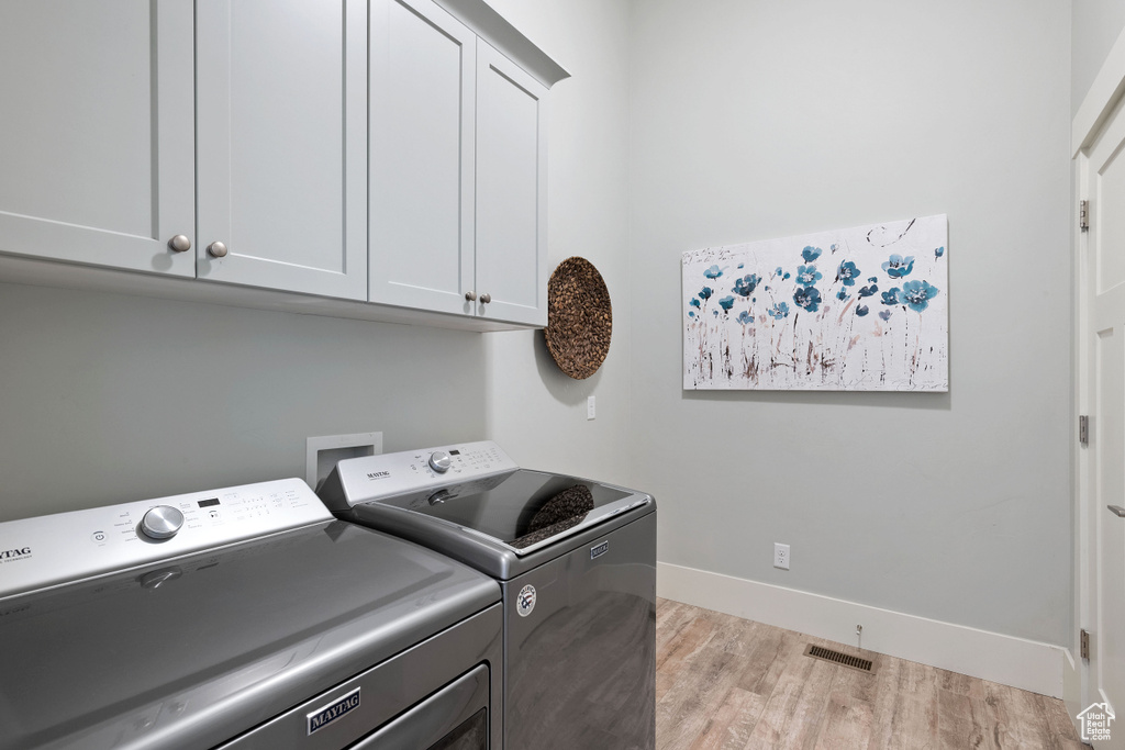 Laundry area with independent washer and dryer, cabinet space, and light wood finished floors