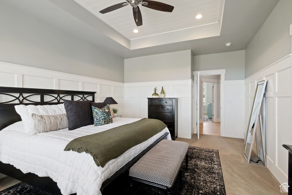 Bedroom with a decorative wall, light colored carpet, a raised ceiling, wainscoting, and recessed lighting