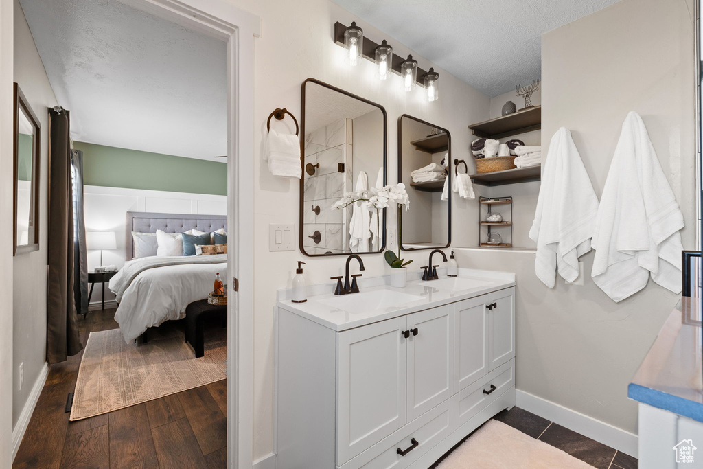 Ensuite bathroom with double vanity, tiled shower, wood finished floors, and a textured ceiling