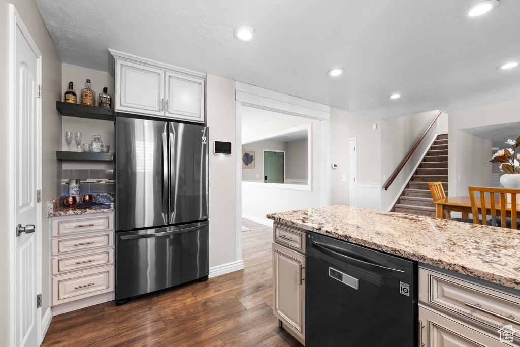 Kitchen featuring freestanding refrigerator, black dishwasher, dark wood-style flooring, open shelves, and light stone counters