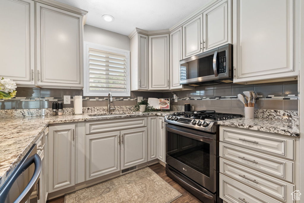 Kitchen featuring appliances with stainless steel finishes, tasteful backsplash, dark wood finished floors, and light stone countertops