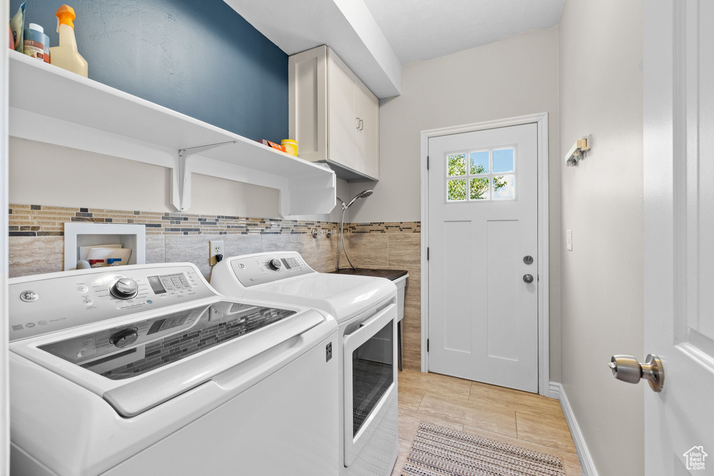 Laundry area with cabinet space, separate washer and dryer, light wood-type flooring, and tile walls