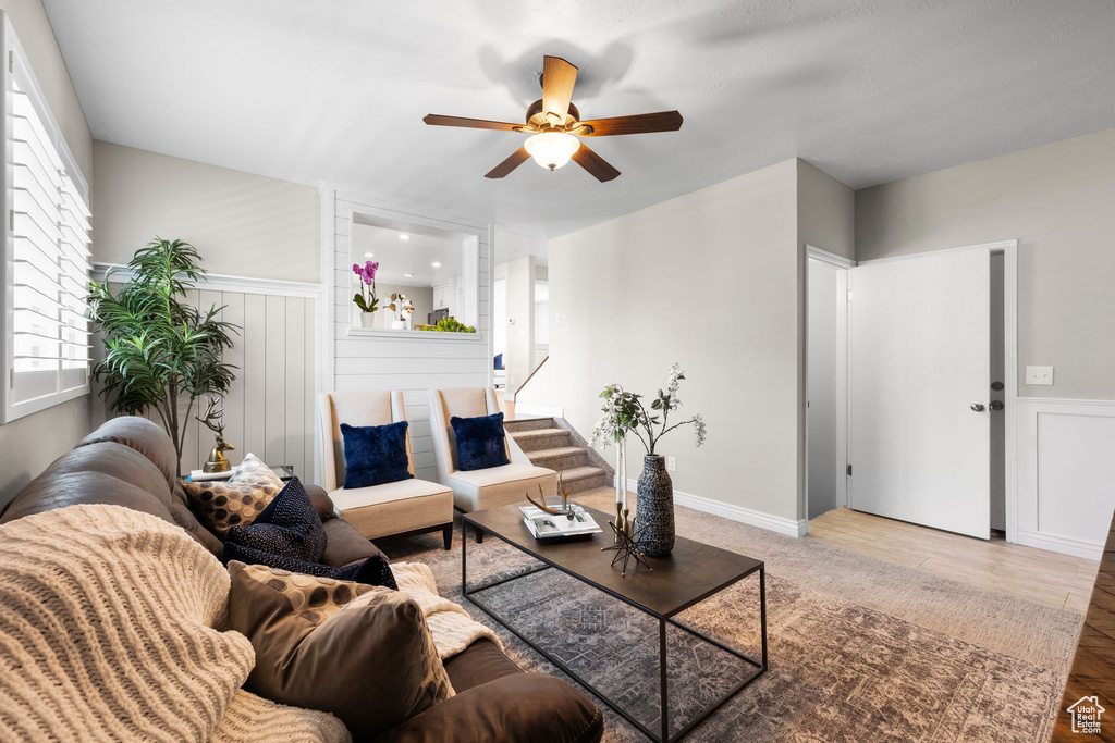 Living room featuring a ceiling fan, stairs, a wainscoted wall, and wood finished floors