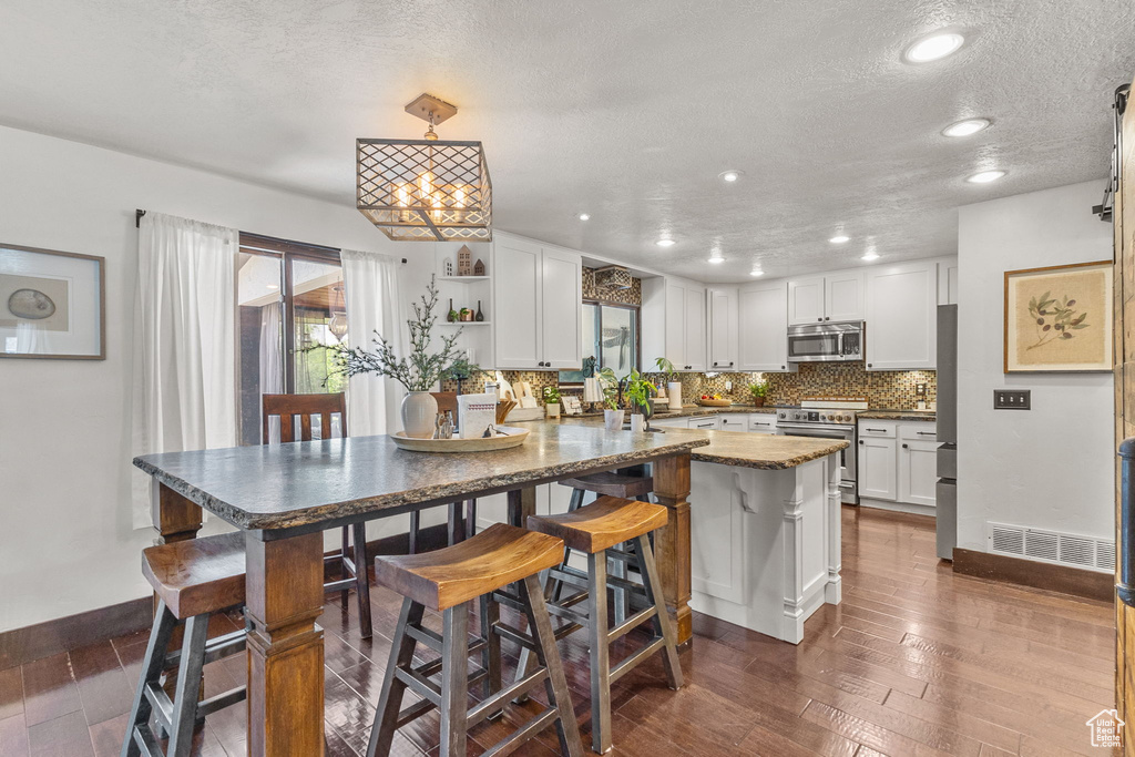 Kitchen featuring stainless steel appliances, dark wood finished floors, white cabinetry, decorative backsplash, and a textured ceiling