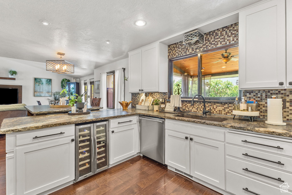 Kitchen featuring dishwasher, beverage cooler, a peninsula, tasteful backsplash, and a textured ceiling
