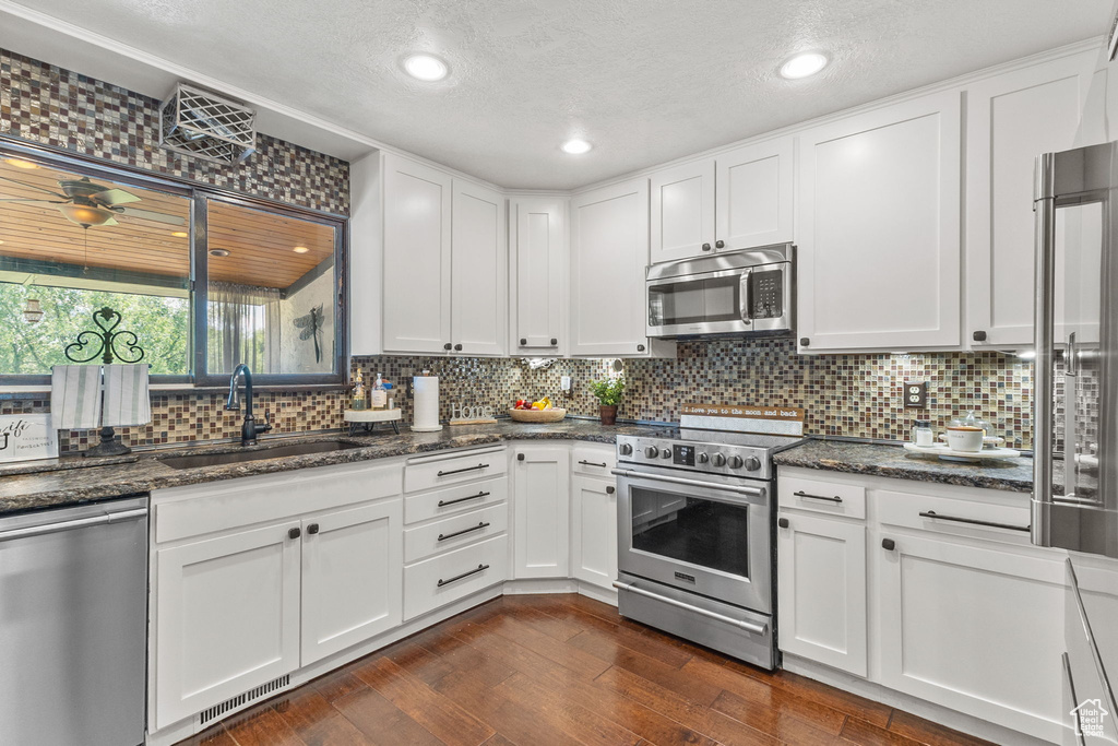 Kitchen featuring appliances with stainless steel finishes, tasteful backsplash, white cabinets, a textured ceiling, and dark stone countertops