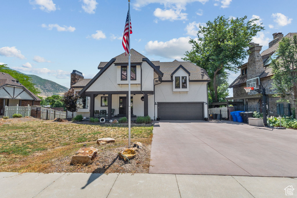 Tudor-style house featuring stucco siding, covered porch, concrete driveway, a chimney, and a shingled roof