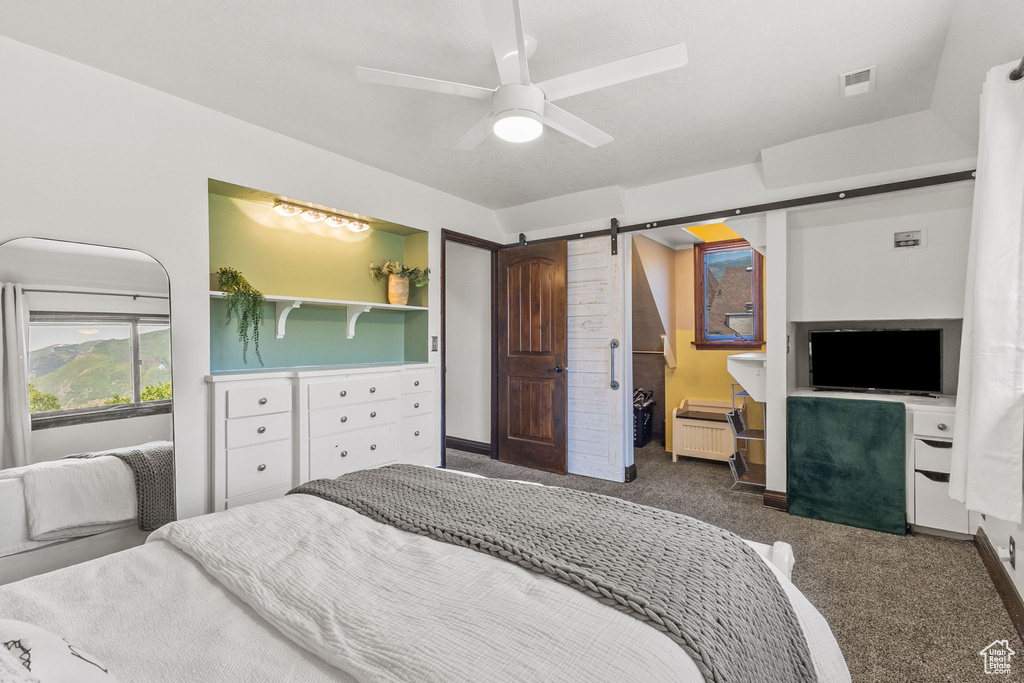 Carpeted bedroom with a barn door and a ceiling fan