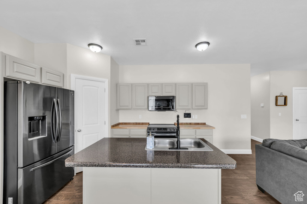Kitchen with stainless steel appliances, dark wood-type flooring, a center island with sink, and open floor plan
