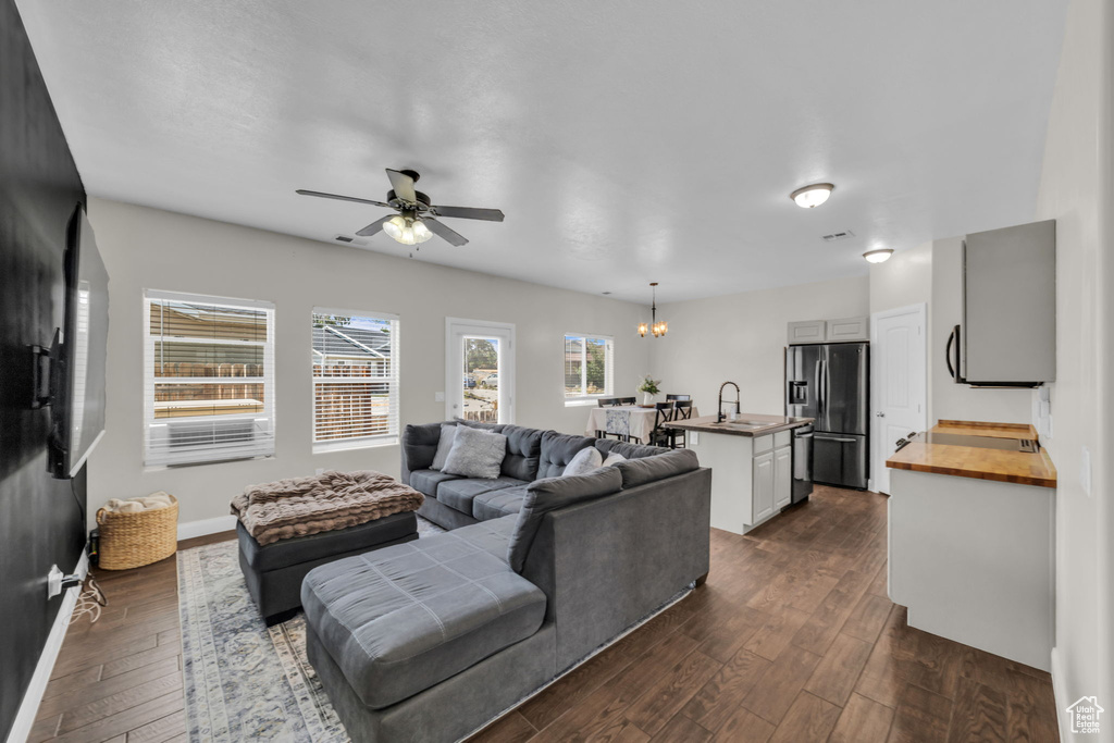 Living room featuring dark wood-style floors, a chandelier, and a ceiling fan