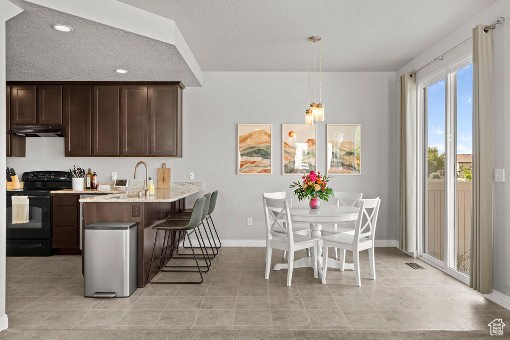 Kitchen featuring black / electric stove, under cabinet range hood, a kitchen breakfast bar, dark brown cabinetry, and a peninsula