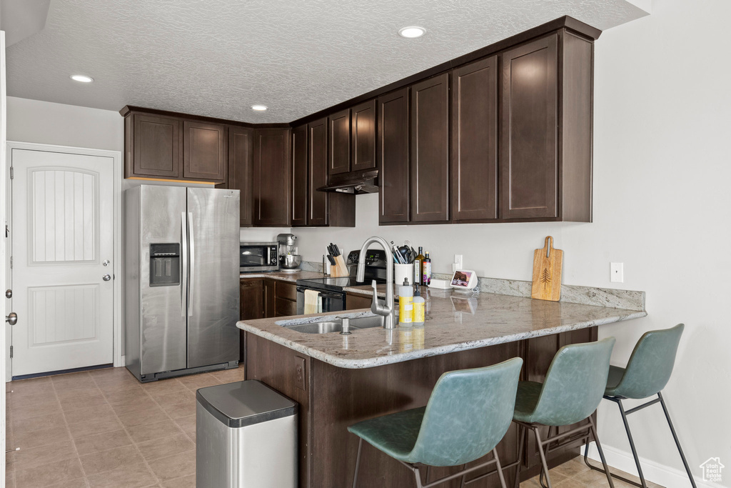 Kitchen featuring stainless steel appliances, dark brown cabinets, a peninsula, under cabinet range hood, and recessed lighting