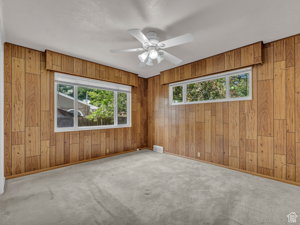 Spare room featuring wooden walls, ceiling fan, and carpet