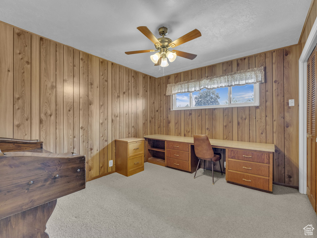 Office area featuring carpet floors, ceiling fan, and wooden walls