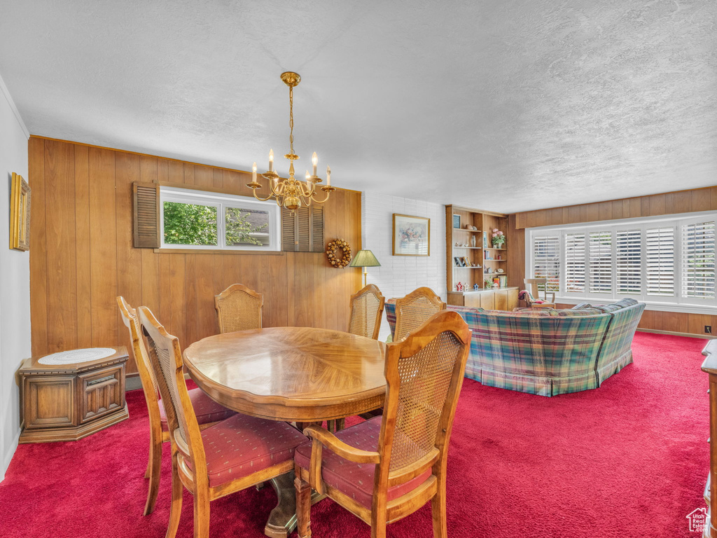 Carpeted dining room featuring wooden walls, a chandelier, and a textured ceiling