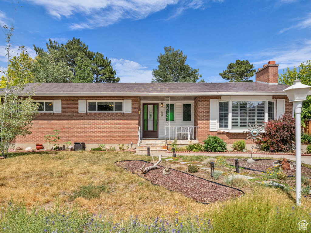Ranch-style home featuring brick siding, a porch, a front lawn, a chimney, and a shingled roof