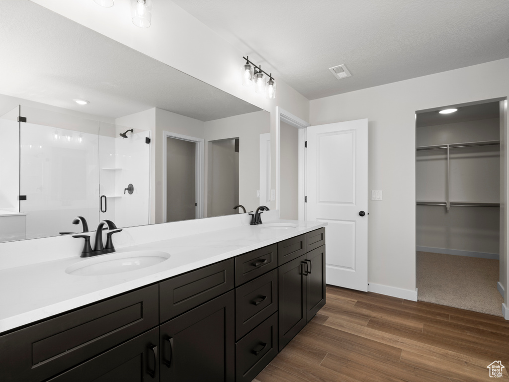 Full bathroom with a stall shower, double vanity, wood finished floors, and a spacious closet