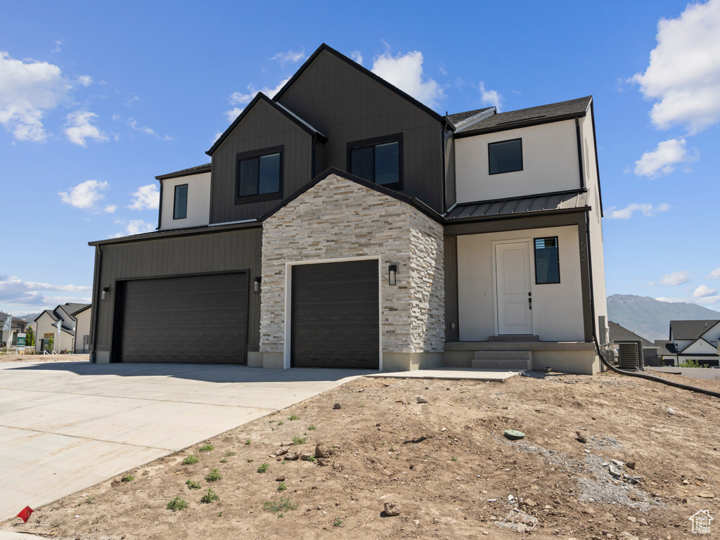 View of front of property featuring stone siding, a standing seam roof, driveway, a metal roof, and an attached garage