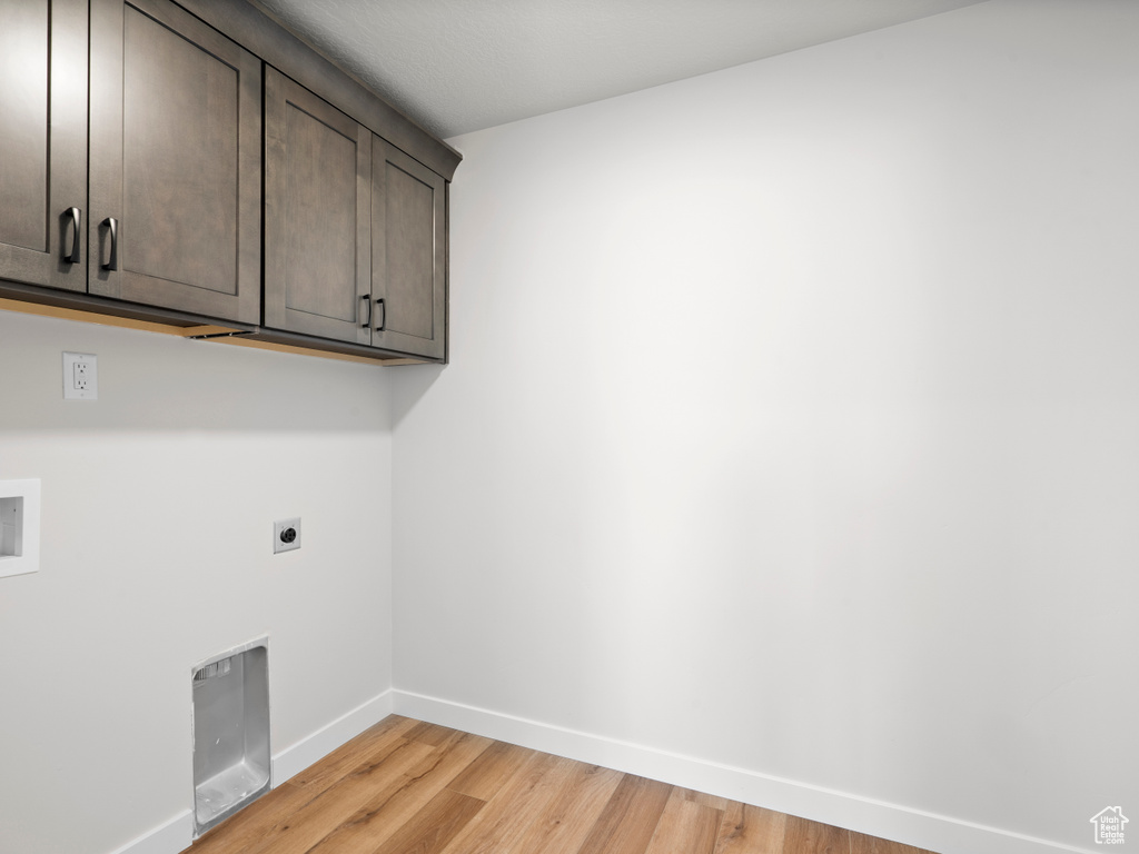 Laundry room with hookup for an electric dryer, cabinet space, and light wood finished floors