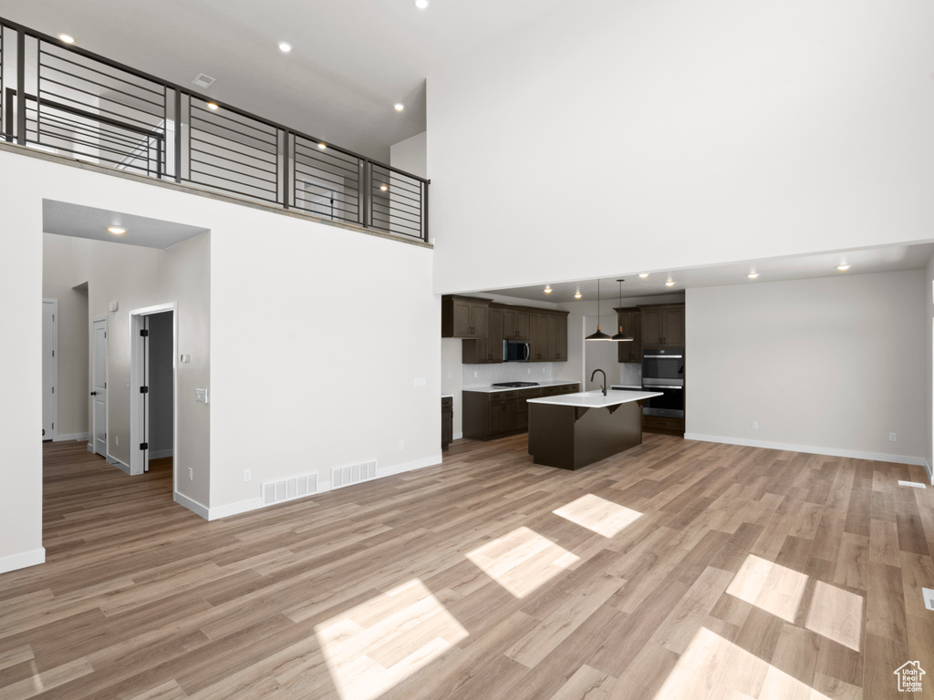 Unfurnished living room with a towering ceiling, light wood-type flooring, and recessed lighting