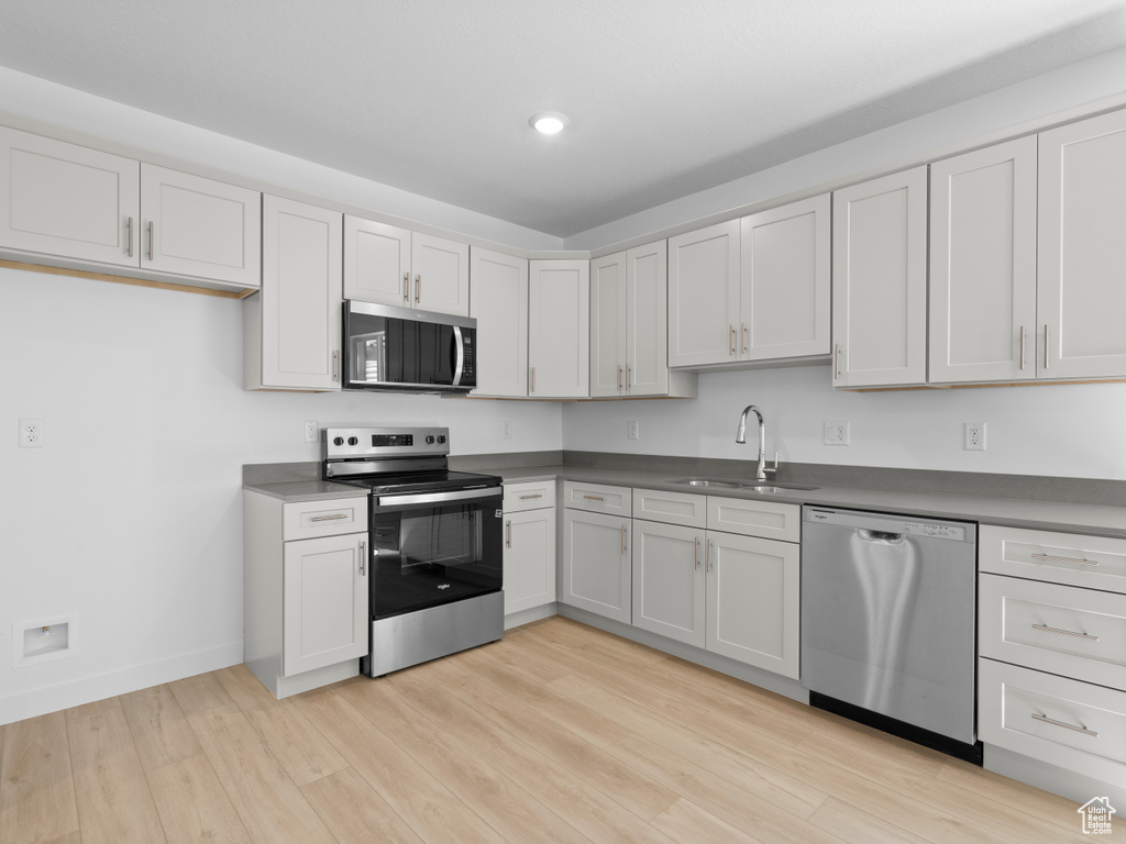Kitchen with stainless steel appliances, light wood finished floors, dark countertops, and recessed lighting