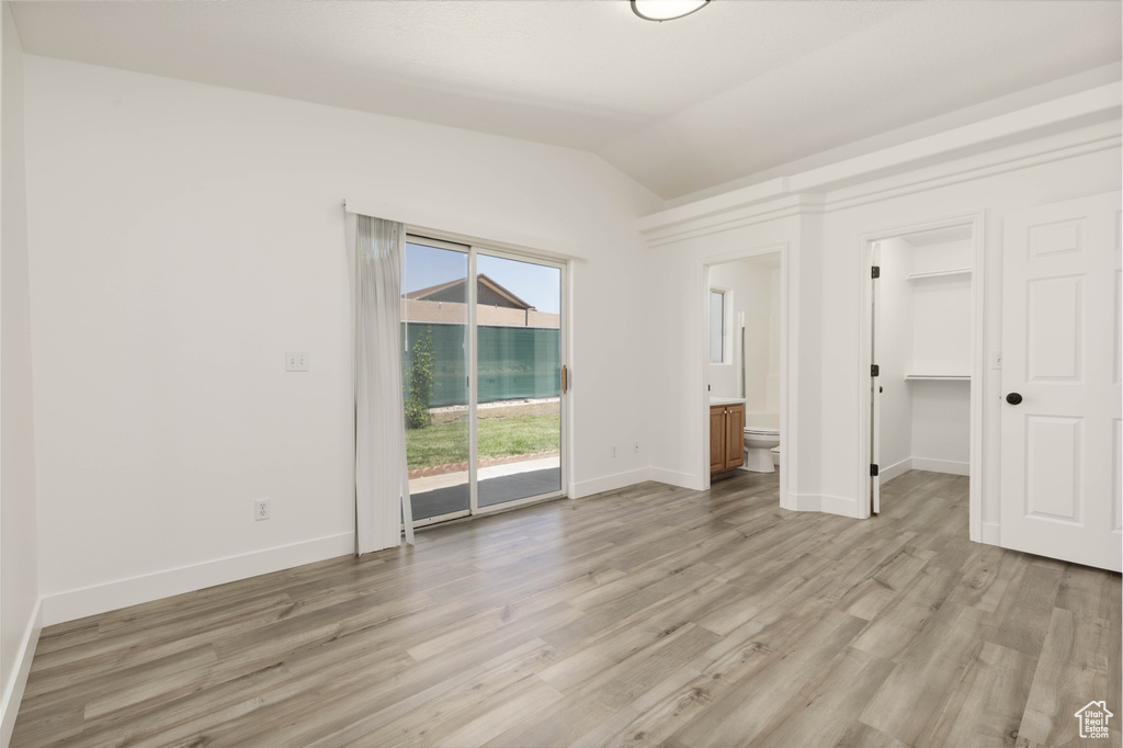 Unfurnished bedroom featuring access to exterior, lofted ceiling, light wood-style flooring, ensuite bathroom, and a walk in closet