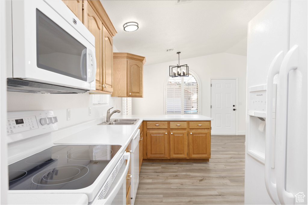 Kitchen with white appliances, light wood-type flooring, a chandelier, vaulted ceiling, and light countertops