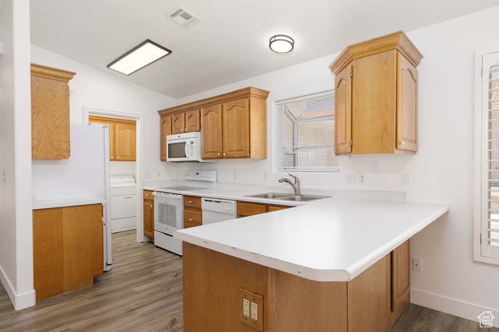 Kitchen featuring white appliances, a peninsula, light wood-type flooring, washer / clothes dryer, and vaulted ceiling