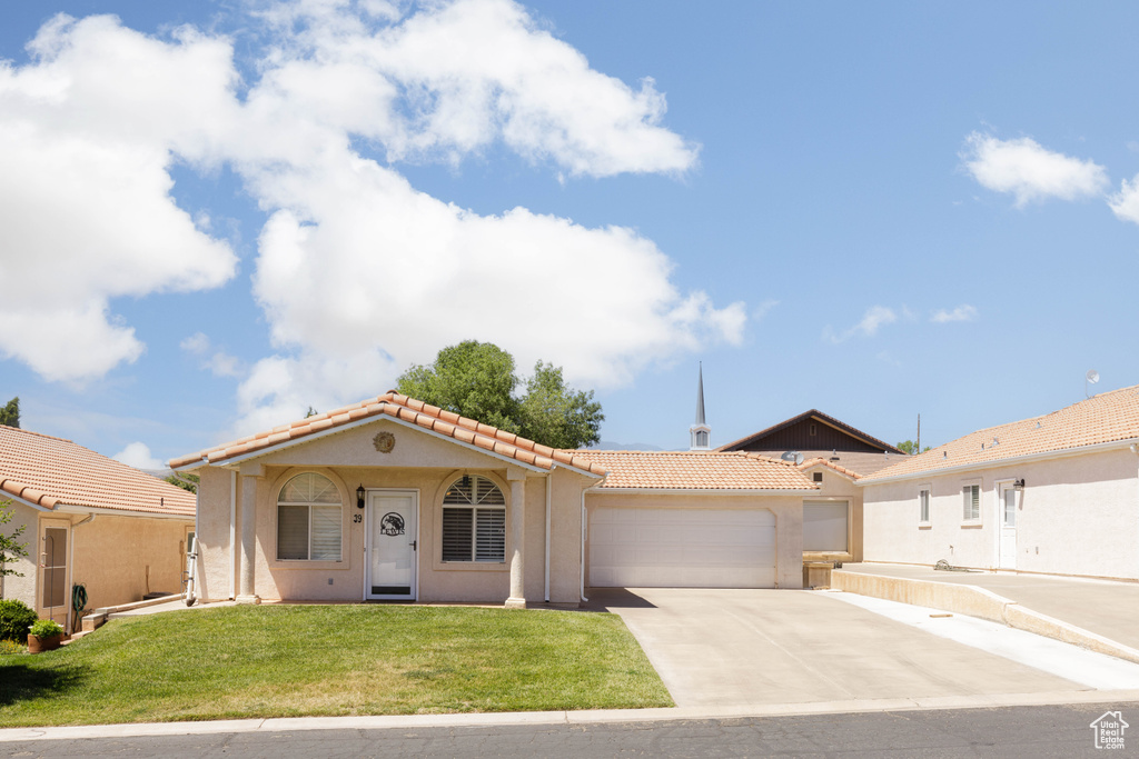 Mediterranean / spanish-style home with a tile roof, an attached garage, stucco siding, concrete driveway, and a front lawn
