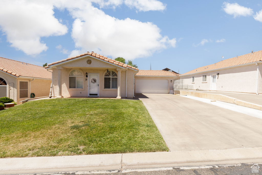 Mediterranean / spanish-style house featuring a tiled roof, driveway, stucco siding, an attached garage, and a front yard