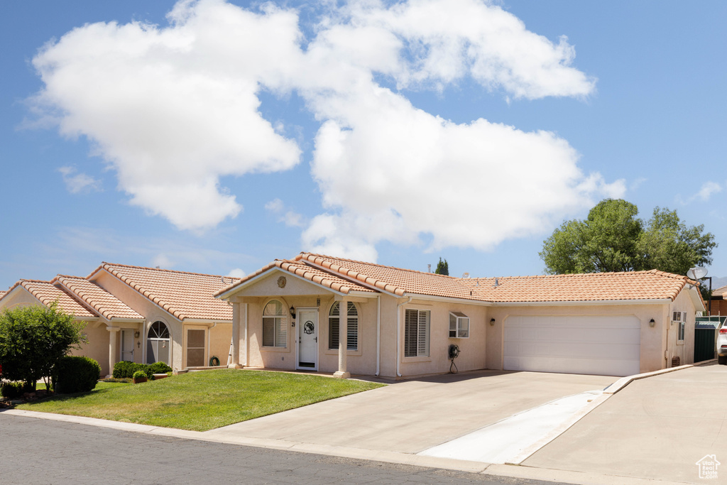 Mediterranean / spanish house featuring an attached garage, stucco siding, driveway, a tile roof, and a front yard