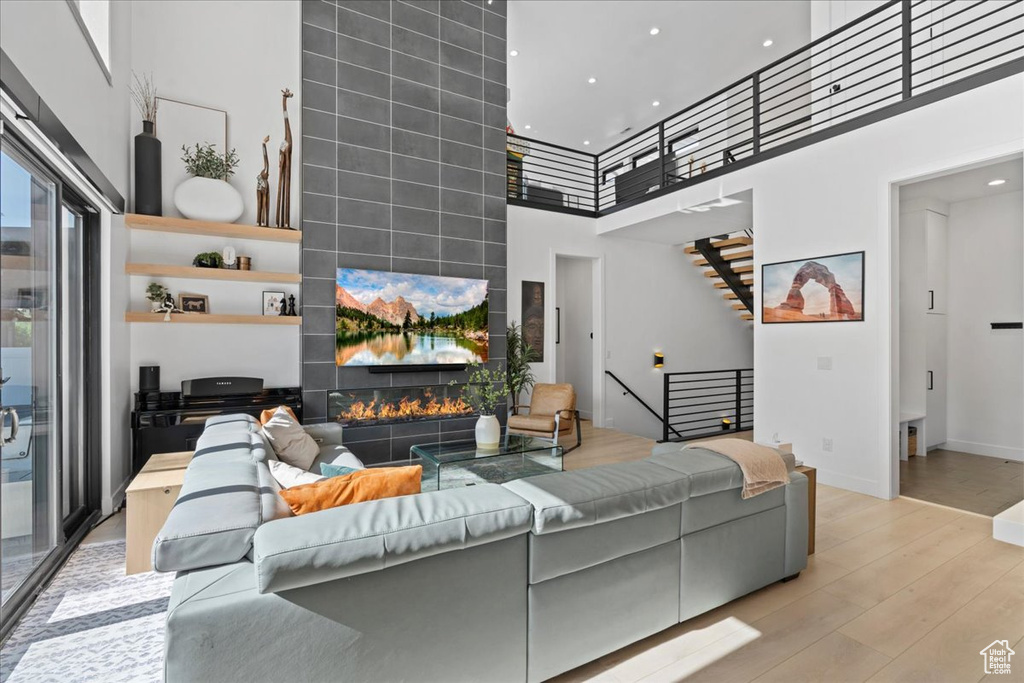 Living area featuring a high ceiling, wood finished floors, stairs, recessed lighting, and a tiled fireplace