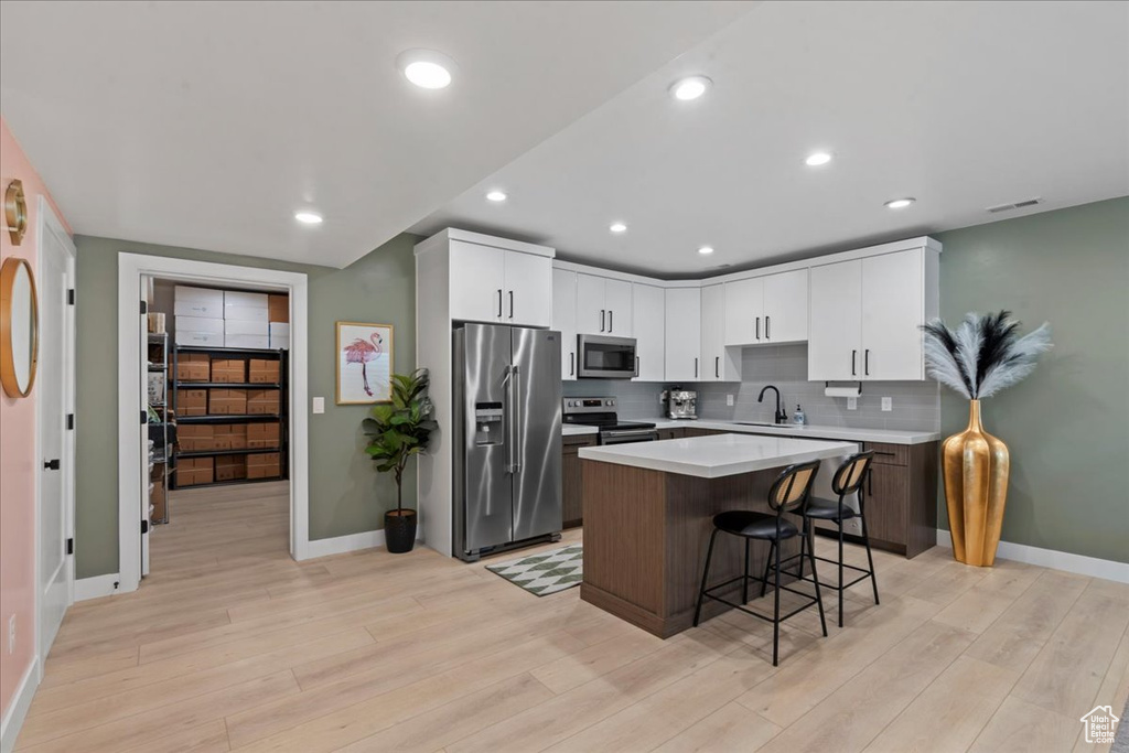 Kitchen featuring stainless steel appliances, a kitchen bar, light wood finished floors, a center island, and light countertops