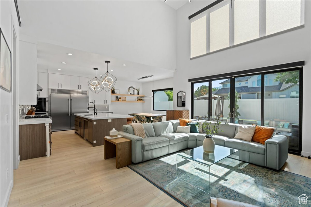 Living area with a high ceiling, a chandelier, light wood-style flooring, and recessed lighting
