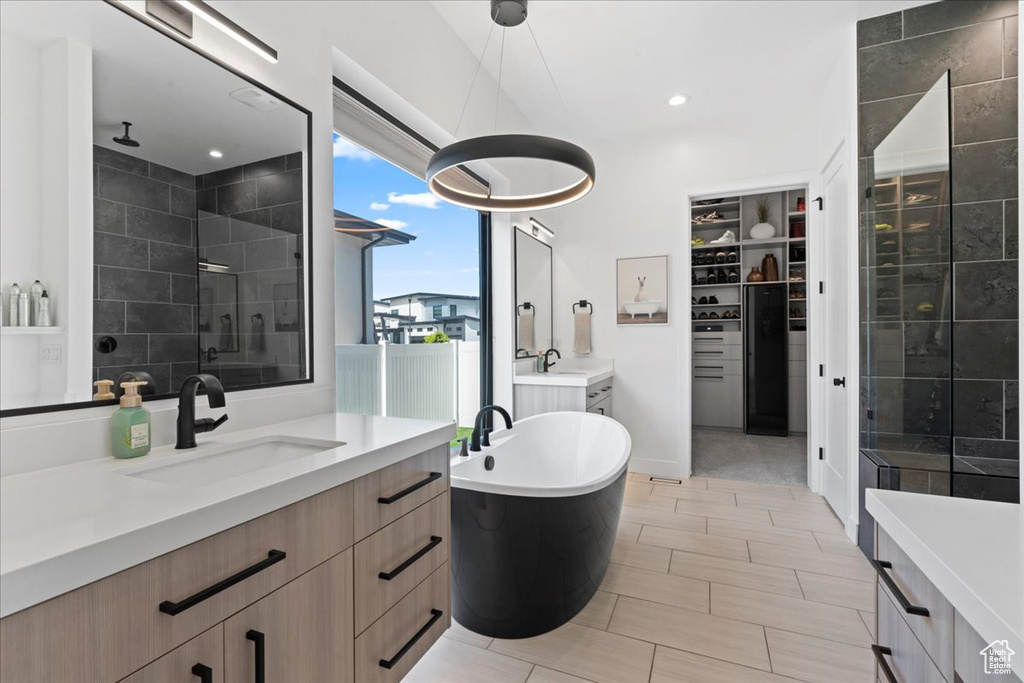 Bathroom featuring two vanities, a stall shower, a freestanding bath, a walk in closet, and recessed lighting