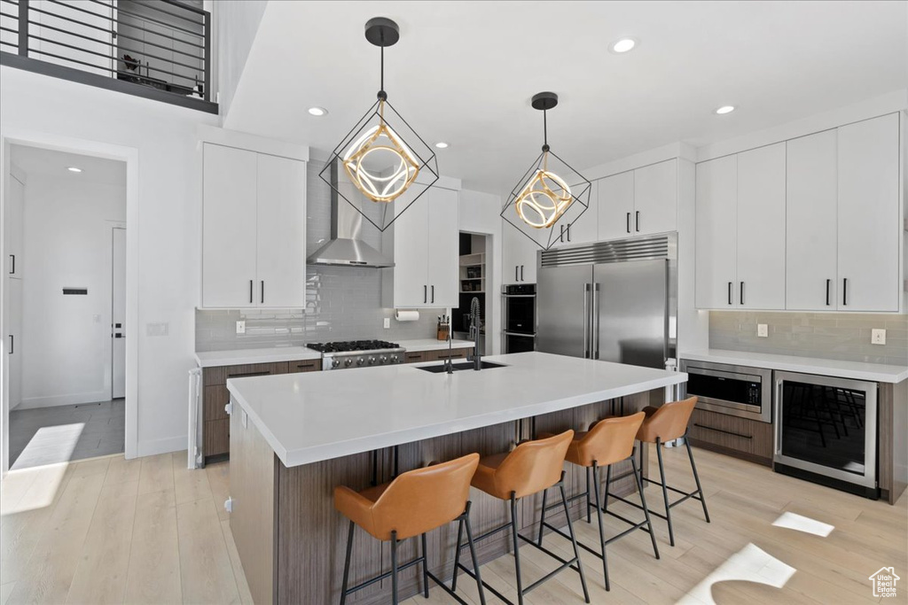 Kitchen with beverage cooler, built in appliances, tasteful backsplash, a breakfast bar, and recessed lighting