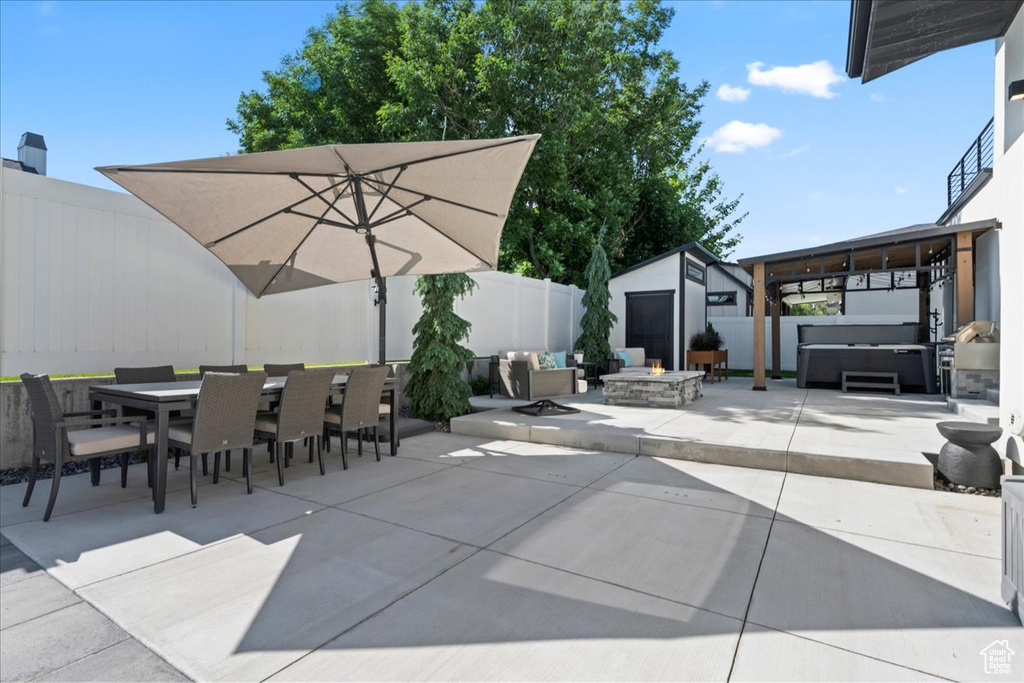 Fenced backyard featuring a hot tub, an outdoor fire pit, a patio, outdoor dining space, and a storage unit
