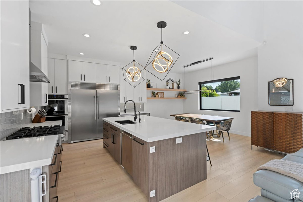 Kitchen featuring appliances with stainless steel finishes, recessed lighting, light countertops, a center island with sink, and light wood-type flooring