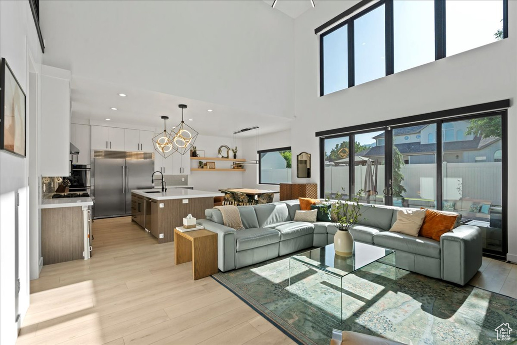 Living area featuring light wood-style flooring, a chandelier, a high ceiling, and recessed lighting