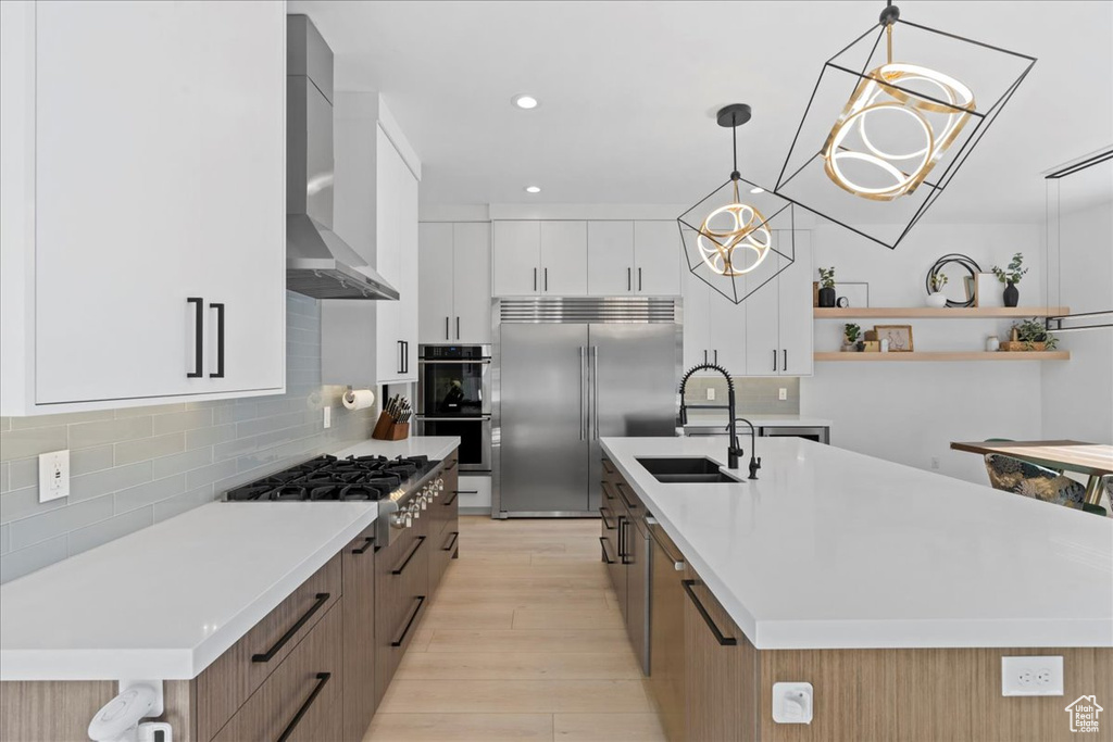 Kitchen featuring stainless steel appliances, wall chimney range hood, light wood finished floors, light countertops, and recessed lighting