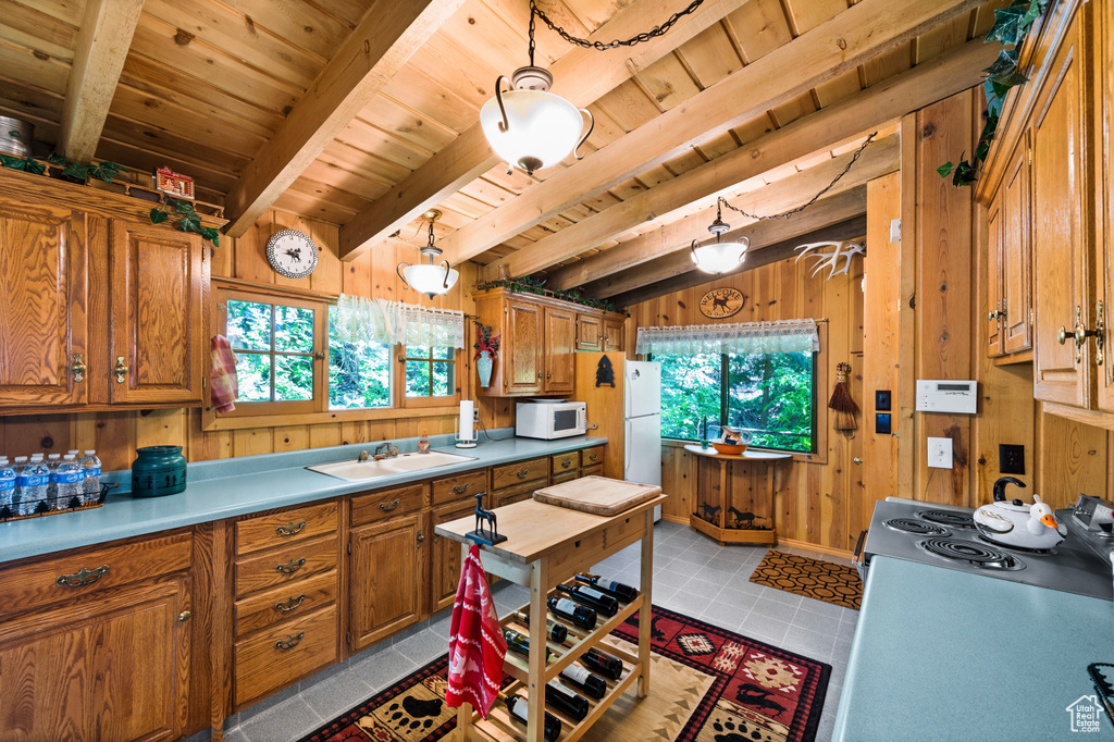 Kitchen with white appliances, a wooden ceiling with exposed beams, plenty of natural light, brown cabinetry, and wood walls