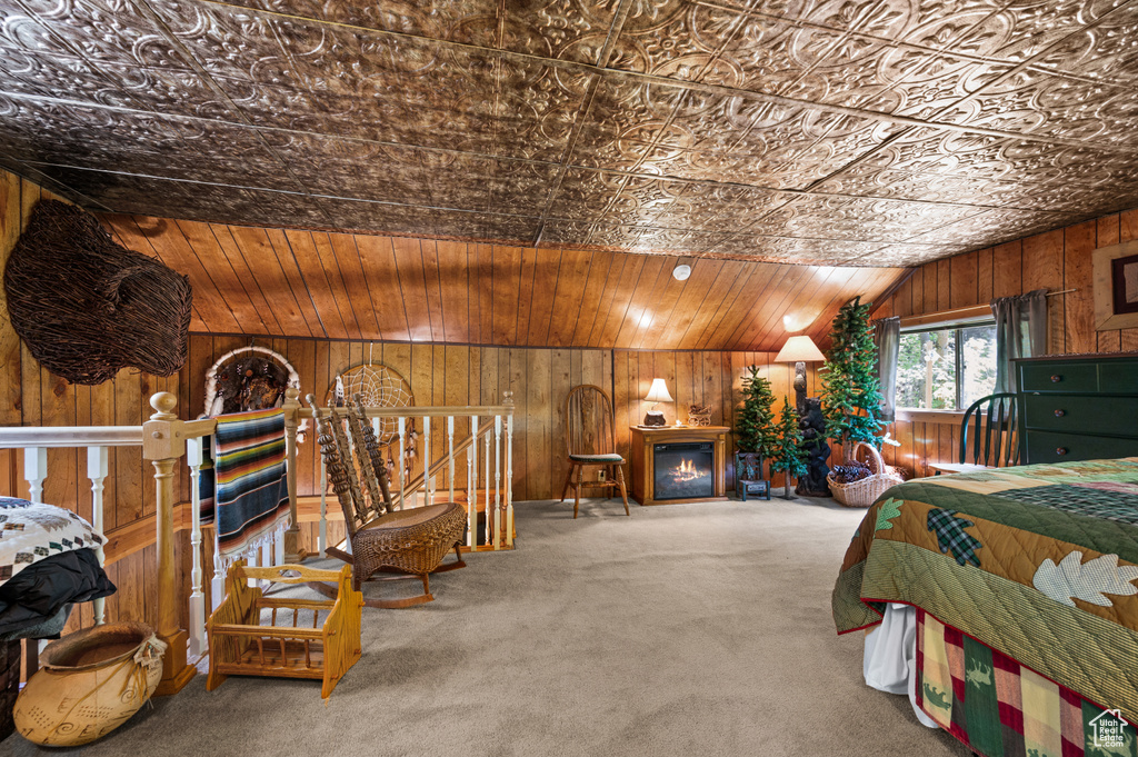 Bedroom with wood walls, carpet flooring, a warm lit fireplace, and vaulted ceiling