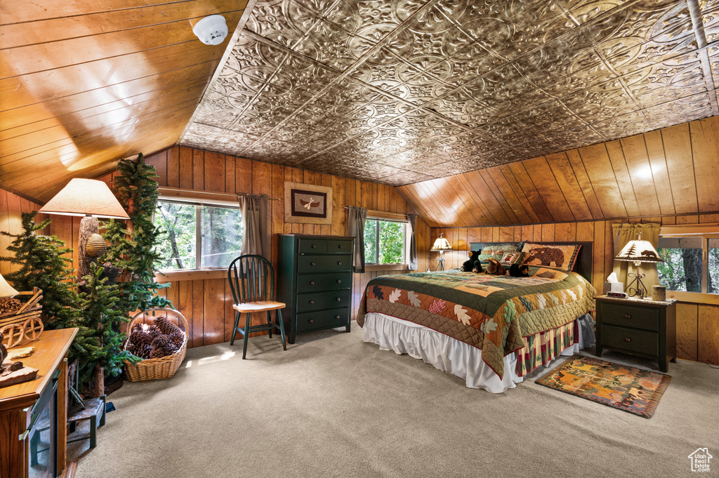 Carpeted bedroom with lofted ceiling, wooden walls, and multiple windows