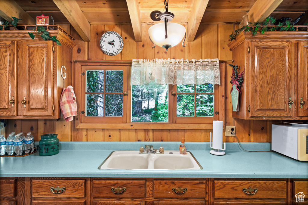 Kitchen featuring wood walls, brown cabinetry, light countertops, a wood ceiling with exposed beams, and plenty of natural light