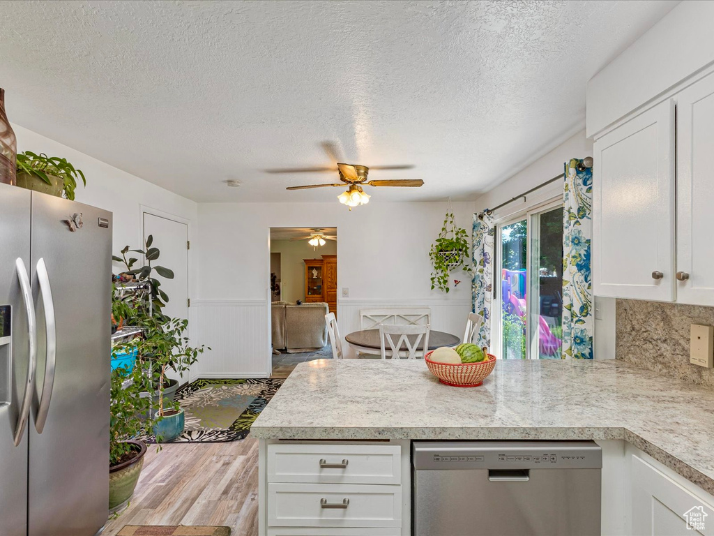 Kitchen with appliances with stainless steel finishes, a peninsula, wood finished floors, a ceiling fan, and light countertops